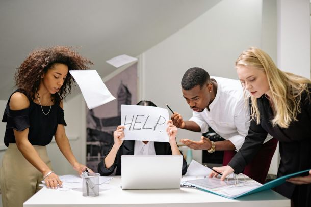 Coworkers brainstorming, one holding a "HELP!" sign